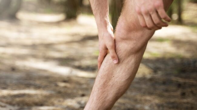 Pijnlijke schenen tijdens wandelen Persoon houdt onderbeen vast tijdens wandeling, mogelijk door pijnlijke schenen na het lopen